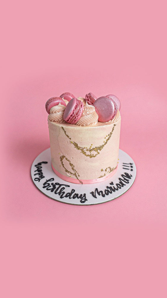 Macaron birthday cake with pink and gold decorations on a pink background