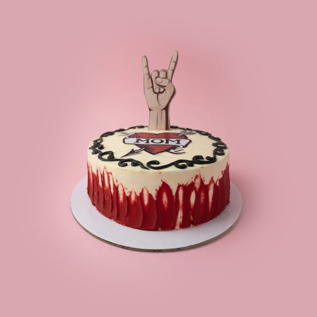 Cake with 'Mom' decoration and hand sign on a pink background