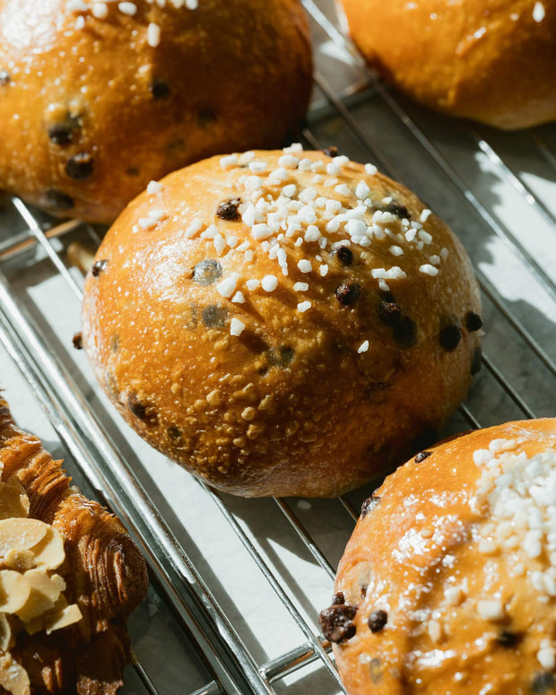 Close-up of bread rolls with sesame seeds and chocolate chips on a cooling rack. Horeca & Foodservice by Flour Girl Bakeries UAE Dubai Abu Dhabi.