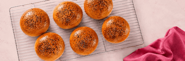 Baked buns on a cooling rack with a pink cloth on a light background