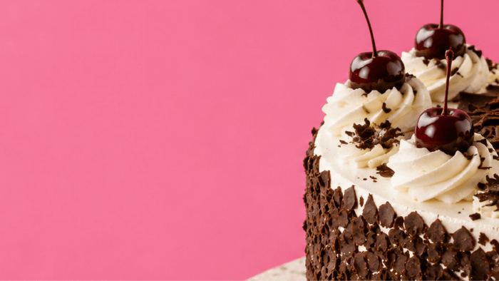 Chocolate cake with white frosting and cherries on a pink background