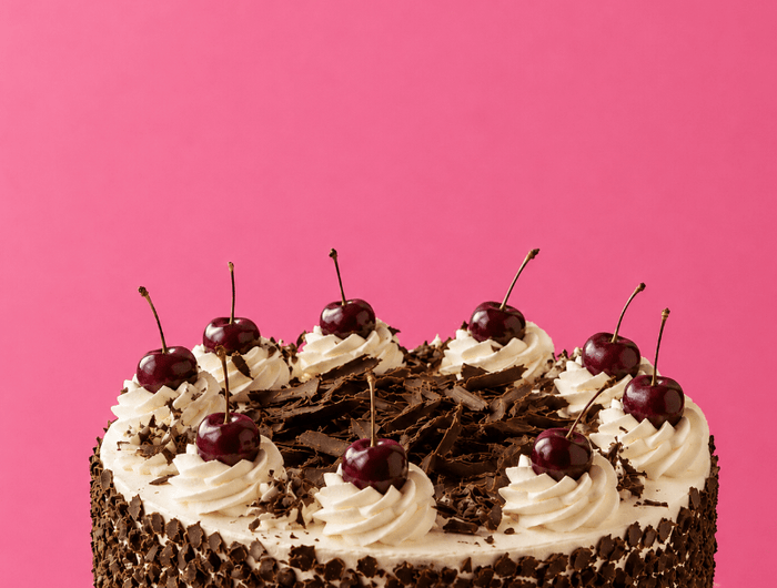 Chocolate cake with white frosting and cherries on a pink background